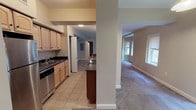 This single-floor residence is designed with an open, flowing layout that connects the main living and kitchen areas seamlessly. The spacious living room is finished with wall-to-wall carpeting and benefits from abundant natural light through multiple windows. A structural column subtly defines the transition between the living space and kitchen without interrupting the open feel.

The kitchen is well-appointed, featuring a mix of light maple and darker wood cabinetry paired with dark countertops. Stainless steel appliances include a dishwasher, refrigerator, and electric range. A central island with pendant lighting overhead adds both workspace and visual interest, while tile flooring provides a practical surface underfoot.

A hallway leads to the private areas of the unit, where carpeted bedrooms offer generous proportions and include closet space. Two bathrooms serve the residence: one features a full tub-shower combo with white subway tile surround and a window for natural light, while the other includes a wide vanity with double sinks, light wood cabinetry, a large mirror, and tile flooring. The overall palette throughout is neutral and cohesive, creating a clean, functional living environment.