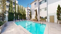Located at 1818 Thayer Ave in the vibrant West Los Angeles neighborhood of 90025, this outdoor amenity space presents a well-appointed pool area designed for relaxation and leisure. The centerpiece is a generously sized rectangular swimming pool with crystal-clear turquoise water, accessed via stainless steel entry rails and framed by a clean, light-toned tile surround. Multiple lounge chairs are positioned poolside, offering ample space to unwind under the Southern California sun.

The courtyard is enclosed by the clean, modern façade of a multi-story building finished in crisp white and gray tones, creating a semi-private, resort-like atmosphere. Tall Italian cypress trees in large concrete planters punctuate the space, providing both vertical visual interest and a natural sense of privacy. Additional potted greenery and low-lying shrubs add to the lush, landscaped ambiance.

A glass-panel balustrade on an upper level overlooks the courtyard, while frosted glass entry doors and a secured gate perimeter ensure controlled access. The combination of contemporary architecture, thoughtful landscaping, and well-maintained recreational facilities makes this outdoor space a standout amenity, ideally suited for the Southern California lifestyle.