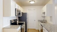 Located at 5959 Cougar Ln in Kearns, Utah, this 2-bedroom, 1-bathroom unit offers a well-designed single-floor layout with a thoughtful mix of comfort and functionality. The open-concept living, dining, and kitchen area forms the heart of the home, bathed in a bright, airy atmosphere with light wood-style flooring throughout. The kitchen is efficiently laid out in a galley style, featuring white cabinetry, granite countertops, a subway tile backsplash, and a full suite of stainless steel appliances including a refrigerator, range, microwave, and dishwasher. A peninsula counter connects the kitchen to the dining and living areas, anchored by a modern chandelier. Both bedrooms are carpeted and receive natural light through window blinds, with the spacious primary bedroom offering generous proportions. Closet space is plentiful, with four closets throughout the unit, including a walk-in closet with wire shelving. The bathroom features a granite vanity, wood-style flooring, and a tub/shower combination. Additional highlights include a dedicated laundry area, a utility room, and a private balcony, making this a complete and practical living space.