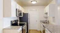 Located at 5959 Cougar Ln in Kearns, Utah, this 2-bedroom, 1-bathroom unit offers a well-designed single-floor layout with a thoughtful mix of comfort and functionality. The open-concept living, dining, and kitchen area forms the heart of the home, bathed in a bright, airy atmosphere with light wood-style flooring throughout. The kitchen is efficiently laid out in a galley style, featuring white cabinetry, granite countertops, a subway tile backsplash, and a full suite of stainless steel appliances including a refrigerator, range, microwave, and dishwasher. A peninsula counter connects the kitchen to the dining and living areas, anchored by a modern chandelier. Both bedrooms are carpeted and receive natural light through window blinds, with the spacious primary bedroom offering generous proportions. Closet space is plentiful, with four closets throughout the unit, including a walk-in closet with wire shelving. The bathroom features a granite vanity, wood-style flooring, and a tub/shower combination. Additional highlights include a dedicated laundry area, a utility room, and a private balcony, making this a complete and practical living space.