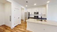 Located at 336 Chestnut Parkway in Indian Trail, NC, this single-floor home offers a clean, contemporary design with thoughtfully selected finishes throughout. Warm wood-look luxury vinyl flooring runs through the main living areas, creating a cohesive and inviting aesthetic from room to room.

The kitchen is a standout feature, showcasing white upper cabinetry paired with slate-gray lower cabinets, a classic white subway tile backsplash, and a granite-topped island with an undermount sink and matte black faucet. Stainless steel appliances, including a French door refrigerator, electric range, and built-in microwave, complete the space. Recessed lighting overhead keeps the area bright and functional.

The open layout connects the kitchen to a spacious living and dining area, offering plenty of natural light through multiple windows. Bedrooms are well-proportioned, with ceiling fans, natural light from windows, and a mix of wood-look flooring and plush carpet underfoot. One bedroom includes direct access to an exterior door, adding versatility to the space.

The bathroom is elegantly appointed with a dual-sink vanity featuring granite countertops, gray cabinetry, a large wall mirror with bar lighting, and a walk-in shower clad in white subway tile with brushed gold and matte black hardware. The overall ambiance is bright, modern, and move-in ready.
