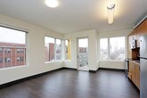 This single-floor urban residence blends modern design with industrial character throughout its well-appointed layout. The kitchen is a standout feature, outfitted with warm wood cabinetry that extends to the ceiling, stainless steel appliances including a range, microwave, dishwasher, and refrigerator, and durable dark hardwood flooring. An exposed metal duct running along the ceiling adds an industrial loft-like aesthetic that carries through the open living area.

The spacious living area is bathed in natural light through a generous arrangement of large windows and a glass door that opens to a balcony, offering views of the surrounding urban skyline and neighboring brick buildings. The dark hardwood floors continue seamlessly through this open space, enhancing the contemporary feel.

The bedroom features plush carpeting and a window with city views, providing a quiet, comfortable retreat. Two bathrooms serve the unit: one equipped with a full soaking tub and shower combination alongside a vessel-style sink and dark countertop, and a second with a walk-in shower stall, both finished with the same rich hardwood-style flooring.

A dedicated laundry area houses a stacked washer and dryer unit with an additional wire shelf, offering practical in-unit convenience. The overall design balances urban industrial elements with clean, neutral finishes throughout.