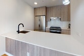 Located at 1277 E 14th St in the Flatbush neighborhood of Brooklyn, NY, this modern single-floor residence showcases a clean, contemporary design throughout. Wide-plank light hardwood flooring runs continuously through the living areas and bedrooms, lending a warm and cohesive feel to the space. The open-concept living area is bathed in natural light through large windows, which also offer views of the surrounding neighborhood. A radiator beneath the windows provides efficient heating.

The kitchen is a standout feature, boasting light wood cabinetry, a generous white quartz peninsula with an undermount sink and matte black faucet, stainless steel appliances including a French door refrigerator and gas range, and a decorative patterned tile backsplash. Recessed lighting illuminates the space effectively.

The bedrooms are bright and well-proportioned, with crisp white walls and ample natural light. The two bathrooms are finished to a high standard: one features a soaking tub with a handheld shower, a wood-tone floating vanity with a white countertop, large-format neutral wall tiles, and distinctive navy penny tile flooring. The second bathroom offers a frameless sliding glass walk-in shower with the same premium tile finishes, providing a spa-like atmosphere throughout.