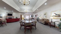 Located on Blue Heron Boulevard in Fond du Lac, Wisconsin, this single-story community facility offers a thoughtfully designed layout with a variety of functional and inviting spaces. The main gathering area is a standout feature, showcasing tray ceilings adorned with elegant brass chandeliers, recessed lighting, and plush carpeting throughout. Multiple round tables with cushioned roller chairs provide ample seating for group activities and socializing, while framed nature and wildlife artwork lends a warm, classic aesthetic to the walls.

A dedicated lounge area offers a more relaxed setting, centered around a stone-surround fireplace topped with a wall-mounted television, complemented by generous red upholstered seating and decorative accents. Adjacent seating nooks with striped armchairs and wood-trimmed interior windows provide quieter spaces for individual relaxation.

The entrance foyer is bright and welcoming, with large exterior windows offering views of the parking area and natural light throughout. Wood-trimmed doorways and warm neutral tones create a cohesive, comfortable atmosphere across all areas.

A well-equipped fitness room rounds out the amenities, featuring cardio machines, a multi-station cable system, free weights, adjustable benches, wall mirrors, and large windows that fill the space with natural light — making it a practical and pleasant environment for exercise.