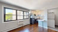 Located at 5536 North Sheridan Road in Chicago's vibrant Edgewater neighborhood, this efficiently designed studio offers a thoughtfully arranged open-concept layout that seamlessly integrates the living, dining, and kitchen areas. Rich hardwood flooring flows throughout, anchoring the space with warmth and continuity.

The kitchen is a standout feature, outfitted with stainless steel appliances including a full-size refrigerator, range, microwave, and dishwasher. White shaker-style cabinetry pairs cleanly with a classic white subway tile backsplash, while dark lower cabinetry adds a modern contrast. A compact peninsula with a white countertop and hairpin legs doubles as a dining surface, making excellent use of the available space.

Natural light enters through multiple windows fitted with wall-unit air conditioning, offering views of the surrounding neighborhood's greenery and urban streetscape. Baseboard heating runs along the perimeter, ensuring year-round comfort.

A set of sleek sliding barn doors leads to a well-appointed bathroom, featuring gray tile flooring, a full soaking tub with floor-to-ceiling white subway tile surround, a white vanity, and matte black hardware accents throughout. The clean, neutral palette and modern finishes give the entire space a fresh, updated feel well-suited to urban living.