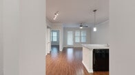 This single-floor residence is designed with an open, cohesive layout that connects the kitchen, dining, and living areas into one flowing space. Rich hardwood-style flooring runs throughout, complemented by crisp white trim, crown molding, and neutral-toned walls that create a clean, modern aesthetic.

The kitchen is a functional centerpiece, featuring dark espresso cabinetry, granite countertops, a peninsula with a built-in sink, pendant lighting, and black appliances including a range, microwave, and dishwasher. A set of built-in shelves near the entry adds practical storage and visual interest.

The living area is spacious and bright, benefiting from multiple windows dressed with white blinds that allow ample natural light. A ceiling fan and track lighting provide versatile illumination, while a secondary door offers direct exterior access.

The bedroom is generously proportioned with crown molding and natural light, and is accompanied by a roomy walk-in closet outfitted with multi-tiered wire shelving. The bathroom includes a dark-toned vanity with granite countertops, a large mirror, and hardwood-style flooring. A dedicated laundry area with an in-unit washer and an electrical panel rounds out this well-equipped space.