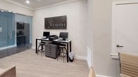 The Reserve on Bayou DeSiard leasing office is a thoughtfully designed single-floor space that blends professional functionality with refined aesthetics. The interior is anchored by a sophisticated lounge area featuring plush upholstered armchairs, layered area rugs, and warm accent lighting, all set against a backdrop of wood-look flooring that adds a sense of warmth and continuity throughout. A standout architectural feature is the striking stacked-wood column paired with floor-to-ceiling glass panel walls, which elegantly partition spaces while preserving an open, airy feel and allowing natural light to flow freely. The business center is equipped with dual computer workstations and a printer, all framed beneath a bold branded wall sign, making it a convenient resource for residents. A cozy private meeting nook offers a round walnut table, upholstered seating, and a locally inspired landscape painting illuminated by pendant lighting—ideal for intimate consultations. Adjacent spaces reveal a fitness center visible through the glass walls, outfitted with exercise equipment and recessed lighting. The overall palette of neutral tones, soft textures, and curated décor creates a polished, welcoming ambiance that reflects the community's upscale character.