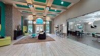 Located at 7400 Steeplecrest Cir in Louisville, KY, this single-story community clubhouse is a striking blend of contemporary design and inviting comfort. The grand lobby immediately impresses with soaring ceilings adorned by a coffered teal-paneled ceiling detail and a series of elegant crystal chandeliers. Large arched windows and glass-paned entry doors flood the space with natural light, while light-toned tile flooring laid in a staggered pattern extends throughout. A comfortable seating area anchored by a plush area rug creates a welcoming gathering zone at the heart of the lobby.

A dedicated lounge area offers a more intimate retreat, highlighted by a sleek modern fireplace framed in stacked-stone tile and flanked by tufted wingback chairs in chartreuse. Bold teal accent walls and equestrian-themed artwork give this corner a distinctive, gallery-like character.

The fully equipped kitchen is a standout feature, showcasing rich dark cabinetry, a textured stone tile backsplash, stainless steel appliances, and a generous granite-topped island with bar seating upholstered in vibrant teal. Sculptural glass pendant lights hang above, adding an artistic touch to the functional space.

Adjacent office areas provide professional workspaces with ample room for meetings and consultations, connected seamlessly to the main common areas through open archways and glass-paneled French doors.