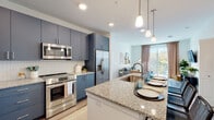 This well-appointed single-floor residence offers a thoughtfully designed open-concept layout that seamlessly connects the kitchen, dining, and living areas. The kitchen is a standout feature, showcasing bold navy-blue cabinetry, a herringbone tile backsplash, stainless steel appliances, and a generous granite-topped island with an undermount sink and pendant lighting overhead — providing both ample workspace and casual bar seating. Warm wood-tone flooring runs throughout the main living area, enhancing the bright, airy ambiance created by recessed lighting and large windows. The living room is anchored by a sliding glass door that opens to a private balcony, filling the space with natural light and offering pleasant outdoor views of the surrounding treetops. The bedrooms are comfortably sized, each featuring large windows with abundant natural light, plush carpeting, and generous closet space, including a walk-in closet. The bathroom continues the navy cabinetry theme with a granite vanity, subway-tiled soaking tub and shower combo, and light wood-look flooring. Additional storage is provided by a spacious walk-in closet with built-in shelving and hanging rods. The overall aesthetic is modern and cohesive, blending contemporary finishes with a clean, neutral color palette throughout.