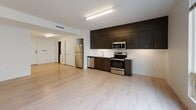 Located at 1939 Dorchester Ave in Boston's Dorchester neighborhood, this single-floor unit offers a clean, modern design throughout. The open-concept layout connects the living area to a well-appointed kitchen, which features dark wood cabinetry extending floor to ceiling, stainless steel appliances including a refrigerator, range, microwave, and dishwasher, and a white countertop with an undermount sink. Light wood-tone flooring flows seamlessly through the main living and kitchen areas, creating a bright and cohesive feel. The living space is generously sized, bathed in natural light from a large horizontal window, and equipped with a wall-mounted mini-split HVAC unit. The bedroom is carpeted for comfort and includes a full-width closet with built-in shelving and hanging rods, providing ample storage. The bathroom is designed with accessibility in mind, featuring grab bars around the tub-shower combo, a toilet, and a dark wood vanity with a white countertop. Clean white walls and contemporary finishes throughout give the unit a fresh, move-in-ready atmosphere well-suited for modern urban living.