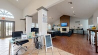 This single-floor leasing office and clubhouse offers a well-appointed, multifunctional space designed to serve both administrative and community purposes. The entry reception area greets visitors with warm terra cotta tile flooring, soaring vaulted ceilings, and an elegant arched transom window above the front double doors, flooding the space with natural light. Decorative columns with crown molding detail define the transition from the reception zone, where glass-top workstations and computer monitors are set up for leasing staff.

The space flows seamlessly into a spacious community lounge area, where rich hardwood flooring, continued vaulted ceilings, and recessed lighting create an inviting ambiance. A dramatic floor-to-ceiling wood-paneled accent wall serves as the focal point, housing a stone-surround fireplace below and a wall-mounted flat-screen television above. Comfortable black leather sectional sofas and a round coffee table furnish the lounge, providing a relaxed gathering area for residents.

Adjacent to the lounge, a pool table adds a recreational element, while pendant lighting overhead enhances the social atmosphere. Additional workspace seating and storage areas are tucked throughout, and windows along the perimeter ensure consistent natural light. The overall design balances professional functionality with approachable, community-centered comfort.