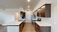 This thoughtfully designed 2-bedroom, 3-bathroom single-floor residence offers a practical and modern living experience. The open living area features warm wood-look hard surface flooring, a ceiling fan, and multiple windows fitted with horizontal blinds that allow ample natural light. A glass door provides direct outdoor access, enhancing the sense of openness. The galley-style kitchen is a standout feature, showcasing rich dark-wood cabinetry, white quartz countertops, a peninsula with an undermount sink, and a full suite of stainless steel appliances including a refrigerator, range, and microwave. Recessed lighting illuminates the space efficiently. Both bedrooms are carpeted for comfort, each equipped with ceiling fans and generous closet space — the primary bedroom notably features dual closets. The three bathrooms maintain a consistent modern aesthetic with dark-wood vanities, white quartz countertops, brushed nickel fixtures, and large mirrors with overhead lighting. Hallways are finished with the same wood-look flooring and include built-in shelving for additional storage. A dedicated laundry room houses a full-size washer and dryer with overhead shelving. Throughout, the residence presents a clean, neutral palette with white walls and bright finishes.