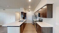 This thoughtfully designed 2-bedroom, 3-bathroom single-floor residence offers a practical and modern living experience. The open living area features warm wood-look hard surface flooring, a ceiling fan, and multiple windows fitted with horizontal blinds that allow ample natural light. A glass door provides direct outdoor access, enhancing the sense of openness. The galley-style kitchen is a standout feature, showcasing rich dark-wood cabinetry, white quartz countertops, a peninsula with an undermount sink, and a full suite of stainless steel appliances including a refrigerator, range, and microwave. Recessed lighting illuminates the space efficiently. Both bedrooms are carpeted for comfort, each equipped with ceiling fans and generous closet space — the primary bedroom notably features dual closets. The three bathrooms maintain a consistent modern aesthetic with dark-wood vanities, white quartz countertops, brushed nickel fixtures, and large mirrors with overhead lighting. Hallways are finished with the same wood-look flooring and include built-in shelving for additional storage. A dedicated laundry room houses a full-size washer and dryer with overhead shelving. Throughout, the residence presents a clean, neutral palette with white walls and bright finishes.