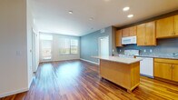 This single-floor residence offers a thoughtfully designed open layout that seamlessly connects the kitchen and living areas. The kitchen serves as a central hub, featuring warm honey-toned cabinetry, granite countertops, and a central island that provides additional prep space and casual seating. White appliances, including a range, microwave, and refrigerator, complement the space, while a teal-accented backsplash adds a subtle pop of color. Recessed lighting illuminates the kitchen, and rich hardwood flooring extends throughout the main living areas, adding warmth and visual continuity.

The living area is bright and open, benefiting from natural light streaming through large windows and a glass door that leads to an outdoor balcony. Vertical blinds offer privacy while maintaining the airy feel of the space. A secondary room, also with hardwood flooring, connects directly to the main living area and provides flexible use.

The bedrooms are carpeted for comfort and each feature windows with vertical blinds, ceiling fans for air circulation, and generous wall space. The bathroom is clean and functional, with matching granite countertops, warm wood cabinetry, an undermount sink, and a tiled shower-tub combination, all set on hardwood flooring.