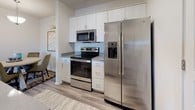 This single-floor residence offers a thoughtfully designed layout that efficiently connects its key living spaces. The living room serves as a central gathering area, finished with plush carpeting and a sliding glass door fitted with vertical blinds that provides access to a private patio, allowing natural light to fill the space.

Adjacent to the living room, the kitchen features stainless steel GE appliances—including a side-by-side refrigerator with ice maker, electric range, and over-the-range microwave—paired with white cabinetry extending to the ceiling and light-toned countertops. Wood-look flooring flows throughout the kitchen and connects to a dedicated dining nook, which is set apart by a pendant light overhead.

The two bedrooms are carpeted and offer a calm, neutral palette. Each room accommodates a full-sized bed comfortably, and the primary bedroom includes a windowed view, a closet with bi-fold doors, and recessed ceiling detail. The bathroom is finished with tile-look vinyl flooring, a shower with curtain enclosure, a vanity, and a window for natural ventilation.

Completing the unit is a dedicated laundry closet housing a full-sized GE top-load washer and dryer with overhead shelving.