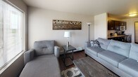 This furnished one-bedroom, one-bathroom unit is laid out on a single floor, offering a functional and cohesive living environment. The open-concept kitchen is a standout feature, equipped with stainless steel appliances including a range, microwave, and refrigerator, complemented by dark espresso cabinetry and granite-style countertops. A dedicated pantry with built-in wire shelving provides ample storage. The kitchen flows naturally into the living and dining areas, which are finished with rich hardwood-style flooring throughout. The living room receives generous natural light through multiple windows and a glass-paneled front door, creating a bright and welcoming atmosphere. It comes furnished with a sectional-style sofa, armchair, and coffee table. The bedroom is carpeted for comfort and features a queen-sized bed, nightstand, and a sliding-door closet with organized shelving. The bathroom includes dark wood vanity cabinetry, a granite-style countertop, a wide mirror with vanity lighting, and hardwood-style flooring. In-unit laundry adds practical convenience. Overall, the unit presents a modern, well-appointed interior with a neutral palette and cohesive design throughout.