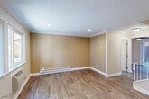 This two-story home offers a practical and well-appointed layout across two floors. The main level hosts the living room, kitchen, and a full bathroom. The living room features warm wood-look laminate flooring, crown molding, recessed lighting, and a baseboard heating system, all beneath a textured ceiling that adds subtle character. Neutral tan walls provide a versatile backdrop throughout the space.

The kitchen is a functional highlight, equipped with stainless steel appliances including a refrigerator, range, microwave, and dishwasher. White shaker-style cabinetry extends to the ceiling, complemented by a mosaic tile backsplash, light stone countertops, and a skylight that fills the room with natural light. A window above the sink overlooks the outdoors.

The upper level contains both bedrooms, a second full bathroom, and a dedicated laundry area. The generously sized primary bedroom features carpet flooring, dual windows for natural light, a baseboard heater, and a closet with mirrored sliding doors. The shared bathroom includes a dual-sink vanity with a tile backsplash and ample cabinetry. The in-unit laundry area houses a stacked washer and dryer alongside built-in shelving for additional storage.