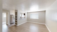 This single-floor unit offers a well-planned layout with a clean, updated aesthetic throughout. The open-concept living area is anchored by light wood-look flooring, neutral gray walls, and a textured ceiling, creating a bright and airy atmosphere. A pass-through window connects the living space to the kitchen, while a built-in open shelving unit adds a functional architectural detail to the dividing wall. Natural light enters through a blinds-fitted window, enhancing the spacious feel of the room.

The galley-style kitchen is well-appointed with white shaker cabinetry, granite-look countertops, a subway tile backsplash, and a stainless steel sink. A window above the counter provides additional natural light, and stainless steel appliances, including a range with overhead microwave, complete the space.

The bathroom features a granite-topped vanity, wood-look flooring, and a tub-shower combination dressed in large-format marble-style wall tile with brushed nickel fixtures, offering a refined finish.

The bedroom is carpeted for comfort and includes a ceiling fan, a window with blinds, and ample wall space, providing a calm and functional retreat within the unit.