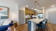 This well-designed single-floor residence offers a seamless blend of modern aesthetics and practical functionality. The open-concept layout connects the kitchen and living area, creating a bright, cohesive space ideal for everyday living and entertaining.

The kitchen is a standout feature, showcasing a large granite-topped island with seating for multiple guests, illuminated by a trio of industrial-style pendant lights. Two-toned cabinetry — warm natural wood uppers paired with slate-grey lowers — adds visual depth, while a white subway tile backsplash provides a clean contrast. Stainless steel appliances, including a refrigerator, range, microwave, and dishwasher, complete the well-equipped kitchen.

The living area benefits from generous natural light through large windows and a glass door that opens to a balcony with outdoor views. Rich wood-tone flooring runs throughout, anchoring the space with warmth, while a ceiling fan adds comfort.

The bedroom is a calm retreat, featuring a large window with views to the surrounding area and ample room for furnishings. The full bathroom includes granite countertops, dark cabinetry, and a bathtub-shower combination. A stacked washer and dryer unit provides convenient in-unit laundry. Together, these spaces form a cohesive, modern residence with thoughtful finishes at every turn.