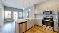 Located at 30 Market St SW in Concord, NC, this 2-bedroom, 2-bathroom residence offers a well-designed single-floor layout that makes efficient use of its space. The kitchen is a standout feature, showcasing granite countertops, light wood-tone cabinetry, a suite of stainless steel appliances including a dishwasher, range, microwave, and refrigerator, and stylish pendant lighting. The kitchen flows openly toward the living area, which benefits from natural light through large windows. Wood-style flooring runs throughout the main living and kitchen areas, adding warmth and continuity to the space. Both bedrooms are finished with plush carpet and neutral gray walls, and each is served by windows with blinds that bring in natural light. The primary bedroom includes a walk-in closet outfitted with multi-tier wire shelving, providing ample organized storage. A second closet with wire shelving is also available. Both bathrooms are clean and modern, each featuring a tub/shower combination with white subway tile surround, chrome fixtures, and wood-style flooring. A connecting hallway ties the layout together cohesively. The overall aesthetic is contemporary and neutral, offering a move-in-ready environment with consistent finishes throughout.