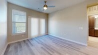 Located at 5640 Prosperity Dr in Garland, TX, this single-story, one-bedroom, two-bathroom residence offers a thoughtfully designed layout that maximizes its compact footprint. The open-concept kitchen and living area serves as the heart of the home, featuring rich dark-toned cabinetry, stainless steel appliances including a refrigerator, gas range, microwave, and dishwasher, along with light quartz countertops and a peninsula with a double-basin sink. Pendant lighting adds a modern touch overhead, while light wood-look flooring flows throughout the main living areas. The living room receives ample natural light through large windows and sliding glass doors fitted with vertical blinds, complemented by a ceiling fan above. The bedroom is carpeted for comfort, includes a ceiling fan, and is served by a walk-in closet with wire shelving for organized storage. Both bathrooms are finished with elegant marble-style tile flooring and surround, with one featuring a full soaking tub and shower combination alongside a dark-cabineted vanity with a white countertop. Clean neutral wall tones and white trim throughout create a bright, cohesive ambiance across the entire space.