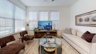 This single-floor residence offers a thoughtfully designed layout that balances functionality with contemporary style. The kitchen is a standout feature, showcasing white flat-panel cabinetry extending to the ceiling, a textured gray tile backsplash, stainless steel appliances including a refrigerator, range, microwave, and dishwasher, and a white quartz countertop island with seating for casual dining. Light wood-tone flooring grounds the space with warmth.

The living area is bright and welcoming, with multiple windows fitted with horizontal blinds that allow generous natural light. A glass-top coffee table and neutral furnishings contribute to the relaxed, modern atmosphere. A glazed entry door with transom window further enhances the sense of openness.

The bedrooms feature plush carpeting, ceiling fans, and windows with views of the surrounding exterior. Each room offers a calm, neutral palette with ample space for furnishings. At least one bedroom includes a walk-in closet.

The bathrooms are clean and functional, with white tilework, undermount sinks, white cabinetry with brushed gold hardware, and a tub-shower combination. Tile flooring completes the polished, cohesive look throughout the home.