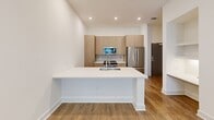 Located at 350 Village Dr in King of Prussia, PA, this one-bedroom, two-bathroom residence offers a well-designed layout with modern finishes throughout. The open-concept kitchen is a standout feature, showcasing light wood cabinetry, white quartz countertops, a large peninsula with an undermount double sink and a sleek coil-spring faucet, a subway tile backsplash, and stainless steel appliances including a range, built-in microwave, and French door refrigerator. Recessed lighting illuminates the kitchen and living areas, which are finished with warm hardwood-style flooring that flows throughout the home. The bedroom is a comfortable, well-proportioned room featuring a ceiling fan, a natural light-filled window with blinds, and access to a walk-in closet. The bathrooms are finished with clean, contemporary styling — one features a soaking tub framed by large-format marble-look tile, a wood-toned vanity, white quartz countertop, and a framed mirror with modern lighting. A dedicated laundry area houses a full-sized Whirlpool front-load washer and dryer, providing added convenience. The overall aesthetic is bright, clean, and modern, with a neutral palette that creates a welcoming and functional living environment.
