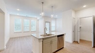 This thoughtfully designed 1-bedroom, 1-bathroom residence offers a bright and modern living experience across a single floor. The open-concept layout seamlessly connects the kitchen and living area, creating an airy, cohesive space bathed in natural light from multiple windows fitted with sleek horizontal blinds.

The kitchen is a standout feature, centered around a granite-topped island with an undermount sink and stainless steel faucet, complemented by a stainless steel dishwasher. Sage-toned shaker-style cabinetry lines the walls, paired with a classic white subway tile backsplash and a full suite of stainless steel appliances including a refrigerator, range, and microwave. Glass pendant lights add a refined touch overhead.

The living area flows naturally from the kitchen, offering an open and versatile space with recessed lighting and light-toned hardwood-style flooring that runs consistently throughout the home. The bedroom is generously sized with windows providing ample natural light and direct access to a dedicated closet and utility room.

The bathroom features a double granite-top vanity with sage cabinetry, brushed gold hardware, and a glass-enclosed walk-in shower with elegant marble-style tile surround. The hallway connects all spaces efficiently, completing a functional and stylish floor plan.