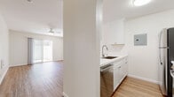 This single-floor residence offers a clean, modern aesthetic throughout, characterized by a bright white color palette, warm hardwood-style flooring, and an abundance of natural light. The open-concept living area is spacious and airy, anchored by a ceiling fan and complemented by views into the kitchen and toward the private outdoor patio.

The kitchen is well-appointed with white shaker-style cabinetry, light countertops, a stainless steel sink with a modern pull-down faucet, a stainless steel dishwasher, a gas range, a refrigerator, and a built-in microwave. The galley-style layout maximizes functionality while maintaining a sleek, cohesive look. An electrical panel is conveniently integrated into the kitchen wall.

The bedroom is generously sized, featuring a ceiling fan, neutral white walls, and sliding glass doors that open directly to a private patio, allowing for seamless indoor-outdoor living and an influx of natural light. The outdoor area is enclosed with a lattice-style privacy wall, creating a comfortable and secluded retreat.

The bathroom is finished in a consistent white tone, offering a combined tub and shower, toilet, vanity with light countertop, and a tall built-in storage cabinet for added convenience. Throughout the entire space, consistent hardwood-style flooring, white trim, and a neutral palette create a harmonious, move-in ready environment.