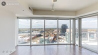 Located in the heart of downtown Durham, NC, this one-bedroom, one-bathroom high-rise unit offers a well-designed open layout with modern finishes throughout. The living room is a standout space, anchored by dramatic floor-to-ceiling windows that span an entire wall, flooding the interior with natural light and delivering breathtaking panoramic views of the Durham skyline and surrounding cityscape. Hardwood flooring extends throughout the main living areas, adding warmth to the contemporary aesthetic.

The kitchen is outfitted with sleek white cabinetry reaching to the ceiling, warm-toned countertops, a subway tile backsplash, and a full suite of stainless steel appliances including a refrigerator with ice and water dispenser, electric range, built-in microwave, and dishwasher. A private balcony accessible from the living area extends the living space outdoors, offering unobstructed elevated views of downtown Durham and beyond.

The bedroom features plush carpeting and direct access to a closet and hallway leading to the bathroom. The bathroom is finished with tile flooring, a wide vanity with white countertop and wood cabinetry, a large mirror with overhead lighting, and clean, neutral tones throughout. A hallway connects the rooms efficiently, completing this thoughtfully designed urban residence.