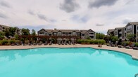 This single-floor amenity space offers residents a comprehensive wellness and recreation experience. The centerpiece of the outdoor area is a generously sized swimming pool with crystal-clear turquoise water, surrounded by a wide sundeck lined with chaise lounge chairs. A wooden pergola structure provides a shaded gathering area along the poolside, while lush landscaping and views of the surrounding residential buildings complete the outdoor ambiance.

Inside, the fitness studio is thoughtfully designed with vaulted ceilings featuring wood-paneled accents and a neutral color palette that creates an open, airy atmosphere. Large windows allow abundant natural light to fill the space while offering views of the pool and courtyard beyond. The studio is divided into functional zones: a yoga and stretching area with floor mats, a rack of colorful kettlebells, and wall-mounted mirrors for form checks, as well as a dedicated cycling zone equipped with multiple stationary spin bikes. A bold, vibrant mural adds an energetic artistic focal point to the main workout area, complemented by storage shelving for accessories and stability balls. Wall-mounted televisions and durable dark flooring throughout complete the practical, motivating environment.