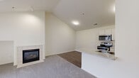 This two-story home offers 3 bedrooms, 2 bathrooms, and a well-designed layout spread across two floors. The main floor forms the larger portion of the home and features an open-concept living room and kitchen area with vaulted ceilings that add a sense of height and openness. The living room is anchored by a tile-surround fireplace and is finished with plush carpet, while the adjoining kitchen area transitions to durable hardwood-style flooring. The kitchen is equipped with stainless steel appliances, including a range, over-the-range microwave, and refrigerator, complemented by white shaker-style cabinetry and light stone countertops. A dedicated laundry room with tile flooring is also located on the main floor. The upper floor houses the bedrooms, including a generously sized primary bedroom with vaulted ceilings, a large arched window, sliding glass doors, and soft carpet flooring that creates a bright, airy retreat. The additional bedrooms also feature vaulted ceilings and carpet flooring. Both bathrooms are finished with tile floors and include a full tub-shower combination with clean white fixtures and vanities with stone-look countertops. Two closets and a hallway complete the home's functional layout.