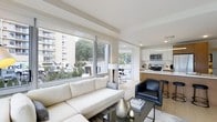 Located at 1133 Warburton Ave in Yonkers, NY, this 2-bedroom, 2.5-bathroom residence offers a thoughtfully designed open-concept floor plan with a clean, contemporary aesthetic. The living area is bright and airy, anchored by large floor-to-ceiling sliding windows that flood the space with natural light and frame views of the surrounding neighborhood and lush greenery. Light-toned walls and flooring create a seamless, cohesive feel throughout. The kitchen flows directly from the living space and features modern white cabinetry, warm wood-toned lower cabinets, stainless steel appliances including a built-in microwave and range, and a sleek countertop with bar seating illuminated by pendant lighting overhead. Recessed lighting throughout adds to the polished, well-lit ambiance. The open layout connects the living, dining, and kitchen areas effortlessly, making the space feel expansive and ideal for both everyday living and entertaining. With two full bedrooms, each supported by their own bathroom, plus an additional half bath, this residence balances comfort and functionality in a modern, move-in-ready package in the heart of Yonkers.