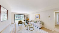 This single-floor residence offers a thoughtfully designed layout across two bedrooms, two bathrooms, and a comprehensive set of living spaces. The bright and airy living room serves as the heart of the home, featuring large sliding glass doors that flood the space with natural light and provide direct views of a lush green outdoor area with a private balcony. Neutral carpet flooring and clean white walls create a versatile backdrop throughout.

The dining room sits adjacent to the living area, featuring a ceiling fan with light fixture and a mirrored wall accent that enhances the sense of space. It connects seamlessly to the kitchen, which is outfitted with white cabinetry, ample counter space, and a stainless steel sink — offering a clean, functional workspace.

The spacious primary bedroom is a comfortable retreat with natural light from wide windows and soft carpeting. The second bedroom is equally versatile, well-suited as a guest room or home office, also benefiting from natural light. Both bathrooms are finished with white vanities, large mirrors, and warm gold-toned fixtures.

Additional highlights include a dedicated in-unit laundry room with stacked washer and dryer, two hallways, and two closets providing practical storage. The overall ambiance is clean, light, and move-in ready.