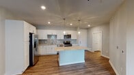 This single-floor residence offers a well-designed layout that balances open-concept living with practical private spaces. The kitchen serves as the focal point of the home, showcasing crisp white shaker-style cabinetry extending to the ceiling, a subway tile backsplash in soft gray tones, and a full suite of stainless steel appliances including a French door refrigerator, electric range, built-in microwave, and dishwasher. Light-toned granite countertops complement the cabinetry throughout, while a generously sized center island provides additional prep and seating space. Pendant lighting above the island and recessed ceiling lights contribute to a bright, welcoming atmosphere. Rich wood-look flooring runs throughout the kitchen and living areas, adding warmth and cohesion to the open space.

The bedrooms feature plush wall-to-wall carpeting in a neutral tone, soft sage-gray walls, and ceiling fans with integrated lighting. Natural light filters in through windows, enhancing the airy feel of each room. The walk-in closet is equipped with multi-tiered wire shelving and hanging rods, maximizing storage efficiency. The bathroom presents a clean, all-white aesthetic with a double-sink vanity topped with granite, a full tub-shower combo, and tile flooring in a neutral stone-inspired pattern.