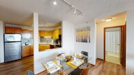 Located at 1300 Harmon Pl in Minneapolis, Minnesota, this single-floor residence offers a well-organized layout that balances functional living spaces with elevated urban views. The living room is a bright, open area anchored by hardwood-style flooring and a large sliding glass door that leads to a private balcony, framing sweeping views of the Minneapolis skyline. Natural light flows generously through the space, enhancing its airy, comfortable ambiance.

The kitchen is efficiently designed with warm oak cabinetry, granite countertops, a mosaic tile backsplash, and a full suite of appliances including a stainless steel refrigerator, electric range, built-in microwave, and dishwasher. Track lighting illuminates the space effectively. A pass-through opening connects the kitchen to the adjacent dining area, where there is ample room for a full dining table, making the layout ideal for entertaining.

The bedroom features plush carpeting and a window with city views, providing a quiet retreat. Two bathrooms are appointed with granite vanity countertops, light wood cabinetry, large mirrors, and tile flooring. Throughout the residence, the consistent use of warm-toned finishes and thoughtful lighting creates a cohesive and inviting atmosphere.