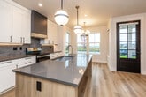 This thoughtfully designed single-floor home blends modern aesthetics with functional living. The open-concept kitchen is a standout feature, showcasing white shaker cabinetry paired with two-toned upper cabinets in a rich charcoal finish, a gray quartz waterfall island with an undermount sink, stainless steel appliances, and a subway tile backsplash. Globe pendant lights and a chandelier illuminate the adjoining dining nook, which is bathed in natural light from a large bay of windows overlooking a lush green landscape. A dedicated pantry area provides generous built-in shelving for additional storage. Conveniently integrated in-unit laundry is tucked neatly beside the kitchen. The bathrooms are finished with marble-look porcelain tile, featuring a frameless sliding glass shower with matte black hardware and built-in niches in one bath, and a soaking tub with full surround tile in another, both with warm wood-toned vanities and gray countertops. The carpeted bedrooms offer a soft, comfortable feel, each with natural light from well-placed windows and sliding or panel-style closets for ample storage. Light hardwood flooring flows through the main living and kitchen areas, tying the space together with a warm, cohesive tone throughout.