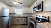 Located at 200 Knollridge Ct in Fairfield, Ohio, this thoughtfully updated single-floor residence offers a cohesive blend of modern finishes and functional design across all rooms. The kitchen serves as a standout feature, showcasing two-tone cabinetry with crisp white upper cabinets and gray lower cabinets, all accented by matte black hardware. Granite countertops, a classic white subway tile backsplash, and a full suite of stainless steel appliances — including a range, over-the-range microwave, dishwasher, and refrigerator — complete this well-appointed space. A ceiling fan with lighting and a window with blinds add comfort and natural light. The bedrooms feature neutral gray walls, wood-look vinyl plank flooring, and windows that allow natural light to filter in. One bedroom includes a spacious closet with built-in shelving and rod. The bathrooms are clean and functional, each equipped with a tiled tub-shower combo, white vanity, and wood-look flooring. A dedicated laundry area provides washer and dryer hookups alongside upper white cabinetry for additional storage, finished with tile flooring. Consistent wood-look plank flooring and a neutral color palette tie the entire space together, creating a cohesive and move-in-ready environment.
