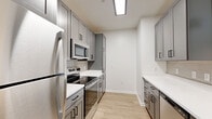 Located in Dale City, Virginia, this well-designed 2-bedroom, 2-bathroom single-floor home offers a clean, modern aesthetic with thoughtful finishes throughout. The open-concept living room welcomes you with light wood-look flooring, crisp white walls, and natural light from window blinds, creating a bright and airy atmosphere.

The kitchen is a standout feature, showcasing gray shaker-style cabinetry with matte black hardware, white quartz countertops, and a neutral tile backsplash. Stainless steel appliances — including a range, microwave, refrigerator, and dishwasher — line both sides of the galley-style layout, maximizing functionality. A kitchen island with a undermount sink and pendant lighting adds both style and convenience, seamlessly connecting to the living area.

Both bedrooms are carpeted for comfort, with the generously sized primary bedroom offering access to a walk-in closet fitted with wire shelving for ample storage. The bathrooms mirror the kitchen's design language, featuring gray vanity cabinetry, white quartz countertops, and matte black fixtures, with a tub-shower combination in each. Light wood-look flooring extends through the bathrooms, tying the home's palette together cohesively.