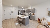 Located at 105 S Main St in Layton, Utah, this single-floor, one-bedroom, one-bathroom residence offers a thoughtfully designed layout with modern finishes and efficient use of space. The open-concept kitchen and living area serves as the heart of the home, anchored by a large central island with a white quartz countertop and bar seating — ideal for casual dining or entertaining. The kitchen is outfitted with gray cabinetry, stainless steel appliances including a gas range, microwave, refrigerator, and dishwasher, along with a white subway tile backsplash and pendant lighting overhead. Light hardwood-style flooring flows throughout, contributing to a bright and cohesive aesthetic. The living area benefits from natural light through large windows with views of the surrounding area. The bedroom is a comfortable, well-proportioned retreat featuring a window with decorative curtains and ample room for furnishings. The bathroom includes a gray vanity with white countertop, a large mirror, and clean, neutral finishes. A dedicated laundry area houses a stacked full-size washer and dryer unit, and a separate closet provides additional storage. The overall ambiance is clean, modern, and functional, making this a practical and attractive home in a convenient Layton location.