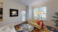 Located at 1316 Town Center Dr in Pflugerville, Texas, this single-story residence offers a thoughtfully designed layout with consistent, quality finishes throughout. The living area greets visitors with rich hardwood-style flooring, elegant crown molding, and generous natural light streaming through large windows with blinds that frame views of the surrounding greenery. The space accommodates comfortable seating and decorative accents in a bright, welcoming atmosphere.

The dining area makes a striking statement with a bold navy accent wall, track lighting overhead, and crown molding that ties the room together. The kitchen is outfitted with dark espresso cabinetry, granite-style countertops, black appliances including a range, microwave, and refrigerator, a tile backsplash, and light tile flooring. A window above the sink allows natural light to fill the workspace.

The bedroom features plush carpeting, crown molding, a ceiling fan, and a large arched window that brings in ample daylight. An additional carpeted room with a window offers flexibility as a study or secondary sitting space. The bathroom is finished with dark cabinetry, granite-topped vanity, tile flooring, and a fully tiled tub-shower surround, completing this well-appointed home.