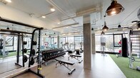 Located at 1601 Broadway in San Diego, this fitness center offers a well-appointed, modern workout facility designed with both function and aesthetics in mind. The space features an industrial-inspired design with exposed ceiling ductwork, concrete structural columns, and a combination of light wood and rubberized flooring that defines distinct workout zones throughout.

The strength training area is equipped with a comprehensive dumbbell rack spanning a full range of weights, multiple adjustable benches, a cable machine, and a power rack, all positioned alongside floor-to-ceiling mirrors that enhance the sense of space. A dedicated functional training zone features artificial turf flooring, a medicine ball rack stocked with various weighted balls, and suspension training equipment, making it ideal for dynamic and athletic workouts.

The cardio section lines the perimeter near expansive floor-to-ceiling windows, offering treadmills and elliptical machines with open views of the surrounding San Diego cityscape. Natural light floods the space throughout the day, creating an energizing atmosphere. Pendant lighting with an industrial character complements the overall design aesthetic.

Additional amenities include wall-mounted TVs, a multi-functional cable and weight machine, and ample open floor space for stretching or bodyweight exercises. The layout is thoughtfully organized to support a full range of fitness activities within a single, cohesive space.