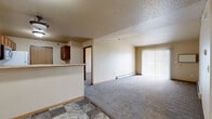Located at 2411 36th St S in Moorhead, Minnesota, this 2-bedroom, 1-bathroom unit offers a practical and comfortable single-floor layout. The open-concept living and kitchen area forms the heart of the home, where a peninsula-style counter with rich cherry wood cabinetry separates the two spaces while maintaining an open, connected feel. The kitchen is well-equipped with a full suite of appliances, including a refrigerator, electric range, and stainless steel microwave, all complemented by ample cabinetry for storage. Stone-look tile flooring runs through the kitchen and entry, while plush carpet extends throughout the living room and bedrooms, adding warmth underfoot. The living room features a large sliding glass door fitted with vertical blinds, allowing abundant natural light and outdoor access. Both bedrooms are carpeted and include windows with blinds, providing comfortable natural light; one bedroom features a full-width sliding closet. Baseboard heating runs throughout the unit, ensuring consistent warmth. The bathroom includes a warm wood vanity with generous counter space, a large mirror with overhead lighting, and matching tile flooring. A textured ceiling is present throughout, lending a classic residential feel to the entire space.