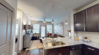 This single-story residence showcases a cohesive modern design highlighted by dark espresso cabinetry, granite countertops, and wood-style plank flooring that flow seamlessly through the main living areas. The open-concept kitchen is well-appointed with stainless steel appliances, including a range, microwave, and refrigerator, complemented by a subway tile backsplash and abundant upper and lower cabinetry. A kitchen island with an undermount stainless steel sink extends into the dining and living space, where sleek pendant lights hang overhead, creating a natural gathering point. The living area is bright and welcoming, benefiting from multiple windows dressed with white blinds that allow ample natural light. A ceiling fan adds comfort, while the entry foyer provides a double-door closet for convenient storage. Both bedrooms feature plush carpeting, ceiling fans, and large windows that fill each room with daylight. The bathroom maintains the consistent design language of the home, featuring granite countertops, dark cabinetry with ample storage, a framed mirror, and wood-style flooring. Overall, the space presents a polished, contemporary aesthetic with practical, well-integrated finishes throughout.
