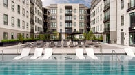Located at 2188 Highland Drive in Salt Lake City, Utah, this contemporary residential community showcases striking modern architecture defined by light brick facades, dark steel accents, expansive floor-to-ceiling windows, and private balconies that frame the building's multi-story presence. At the heart of the property lies a beautifully designed courtyard that serves as the centerpiece of outdoor living.

The resort-style swimming pool is a standout feature, flanked by large-format porcelain tile decking and lined with sleek white and charcoal lounge chairs arranged for both relaxation and socializing. A sophisticated glass panel railing system borders the pool terrace, providing safety while preserving open sightlines. Overhead string lighting adds ambiance to the space during evening hours.

Surrounding the pool, the courtyard extends into thoughtfully landscaped promenades featuring dark metal planter boxes filled with ornamental trees, conical evergreens, and manicured shrubs set against gravel ground cover. A pergola structure provides a shaded gathering spot, complemented by modern benches and seating areas. The backdrop of the Wasatch Mountains is visible beyond the roofline, adding a dramatic natural element to this urban outdoor retreat. The overall ambiance is polished, serene, and inviting.