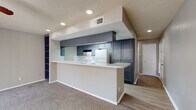 This single-floor residence offers a thoughtfully designed layout that balances open living spaces with functional private areas. The heart of the home is an open-concept kitchen and living area, where a wraparound breakfast bar peninsula serves as both a prep space and a natural divider between the two zones. The kitchen is fitted with gray cabinetry, light quartz-style countertops, a white electric range, a dishwasher, and a refrigerator, all set against a textured backsplash and wood-look flooring. Recessed lighting and a ceiling-mounted ventilation hood complete the culinary space. The adjacent living area is carpeted and benefits from a sliding glass door that invites natural light and provides outdoor access. A built-in shelving unit along one wall adds both character and practical storage. Ceiling fans are present throughout, promoting comfortable airflow in both the living and bedroom areas. The bedroom features plush carpet, a window with blinds, and a wide mirrored sliding-door closet that enhances the sense of space. The bathroom is clean and functional, offering a tiled shower-tub combination, a vanity with matching gray cabinetry and stone-look countertops, and wood-look tile flooring. A textured ceiling is consistent throughout the residence.