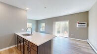 This single-floor residence in Little Falls, MN offers a thoughtfully designed open-concept layout that combines functionality with modern style. The kitchen serves as the centerpiece of the living area, featuring a large island with a double sink, crisp white countertops, dark wood cabinetry, and stainless steel appliances — all flowing seamlessly into the bright, airy living space. Light hardwood flooring runs throughout the main areas, complementing the neutral taupe and gray wall tones. The living room is filled with natural light from multiple windows and a sliding glass door that opens to a private balcony, offering pleasant outdoor views of the surrounding landscape. Both bedrooms are carpeted and well-sized, each with windows that bring in natural light and views of the outdoors, along with baseboard heating and individual wall AC units. The two bathrooms are finished with dark wood vanities, white countertops, and wood-grain tile flooring. The primary bathroom includes an extended vanity with ample cabinetry storage. The secondary bathroom features a full tub-shower combo. A dedicated laundry area with a stacked washer and dryer adds everyday convenience, while a closet provides additional storage. This residence delivers a clean, modern living experience.
