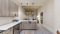 Located at 705 Douglas St in downtown Sioux City, Iowa, this thoughtfully designed 2-bedroom, 2-bathroom unit blends modern aesthetics with industrial character. The open-concept kitchen flows seamlessly into the living area, anchored by sleek flat-front cabinetry in a warm wood-tone finish, crisp white quartz countertops, white subway tile backsplash, and a full suite of stainless steel appliances. A peninsula with an undermount sink and stylish black pendant lighting adds both function and visual interest. The living room impresses with soaring ceilings that expose structural elements, creating an airy, loft-inspired ambiance, and is illuminated by a statement pendant light. The primary bedroom offers generous proportions with elevated ceilings, plush carpet, and ample closet space. The second bedroom is equally well-appointed, featuring a large double-door closet and the same lofty ceiling height. Both bathrooms are finished with clean, contemporary fixtures and tile flooring. A hallway connects the bedrooms to the main living spaces, and a dedicated entryway with a bold dark wood door provides a welcoming arrival. Consistent light gray flooring ties the main living areas together for a cohesive, polished look throughout.