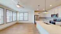 Located at 1001 Boopa Ln in Mount Pleasant, South Carolina, this single-floor residence offers a clean, contemporary design with a bright and cohesive aesthetic throughout. The open-concept living and kitchen area serves as the heart of the home, featuring light hardwood-style flooring, neutral walls, and abundant natural light streaming through multiple windows with horizontal blinds. A ceiling fan enhances comfort in the living area, which also includes sliding glass door access to the exterior.

The kitchen is well-appointed with white shaker-style cabinetry extending to the ceiling, stainless steel appliances including a refrigerator, range, and built-in microwave, a subtle subway tile backsplash, and a large center island with a light quartz countertop and an undermount sink. Stylish pendant lights illuminate the island, adding a modern touch. A dedicated entry hallway provides a clear transition into the main living spaces.

The bedrooms feature plush wall-to-wall carpeting, ceiling fans, and generous windows that bring in natural light and outdoor views. The primary bathroom offers a long double-vanity with quartz countertops, hardwood-style flooring, and a glass-enclosed walk-in shower. The secondary bathroom includes a single vanity and a full tub-shower combination, finished in crisp white tile. The overall ambiance is light, airy, and move-in ready.
