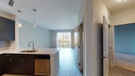 Located at 3000 Dominion Ridge Way in Morrisville, NC, this single-floor residence offers a thoughtfully designed open-concept layout with contemporary finishes throughout. The living area features light hardwood-style flooring and flows seamlessly toward a sliding glass door that opens onto a private balcony, providing outdoor views of the surrounding community. The kitchen is a standout feature, outfitted with dark espresso cabinetry extending to the ceiling, light quartz countertops, a gray subway tile backsplash, and a full suite of stainless steel appliances including a side-by-side refrigerator with water dispenser, electric range with overhead microwave, and dishwasher. A peninsula with pendant lighting connects the kitchen to the main living space, adding both function and style. The bedrooms are carpeted for comfort, each featuring ceiling fans and generous natural light. The primary bedroom includes access to a walk-in closet and an en-suite bathroom. The bathroom is finished with light wood-look tile flooring, a navy blue vanity with white countertop, a large mirror, and a tub-shower combination. The overall ambiance is clean, modern, and move-in ready, with a neutral color palette that complements the bright, light-filled interiors.